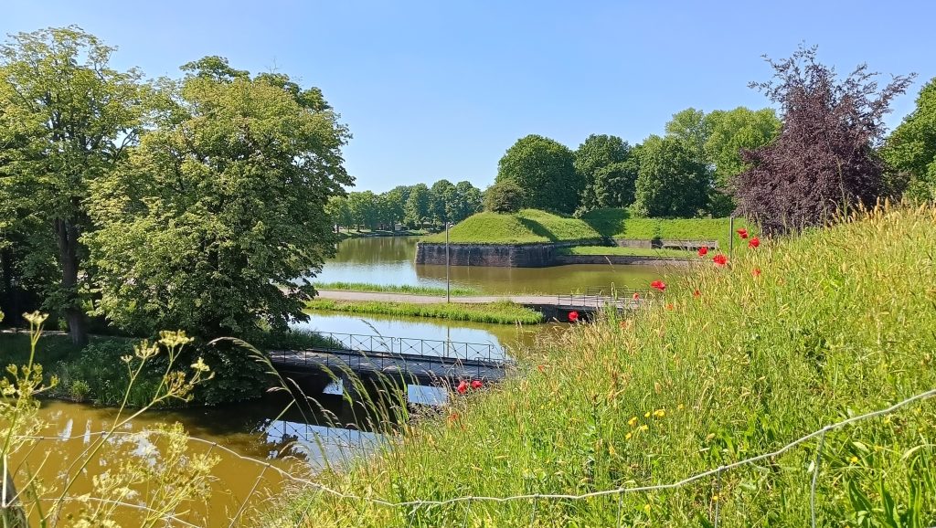 Vestingwerk met gracht, groene wallen en klaprozen langs het wandelpad op een zonnige zomerdag
